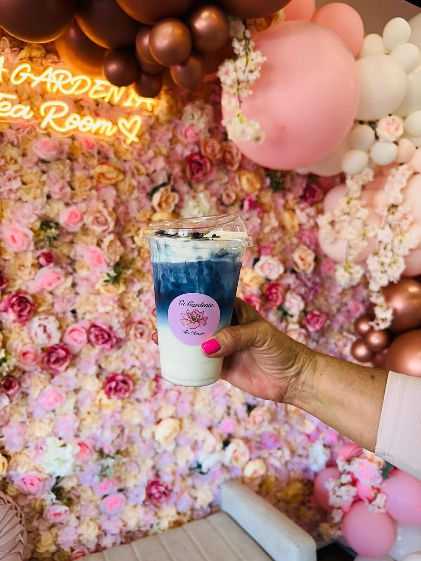 A blue layered tea drink held in front of the tea room flower wall.
