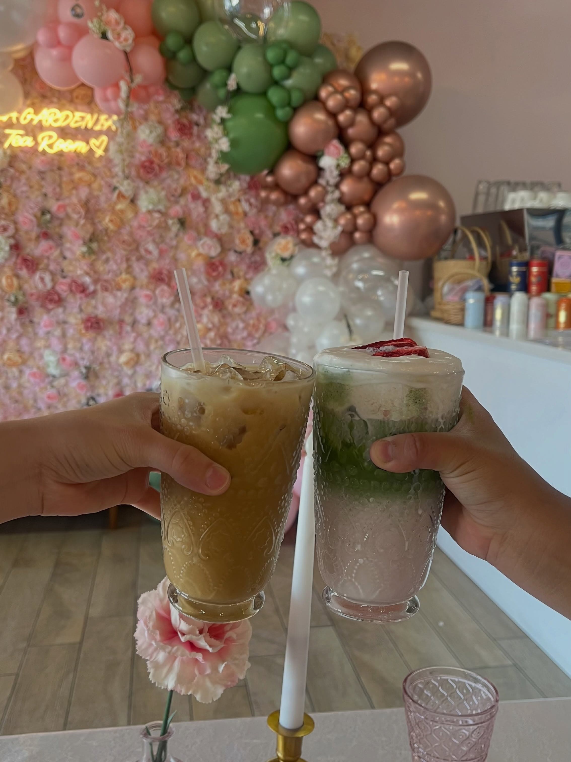 Two iced drinks held together in front of the tea room flower wall.