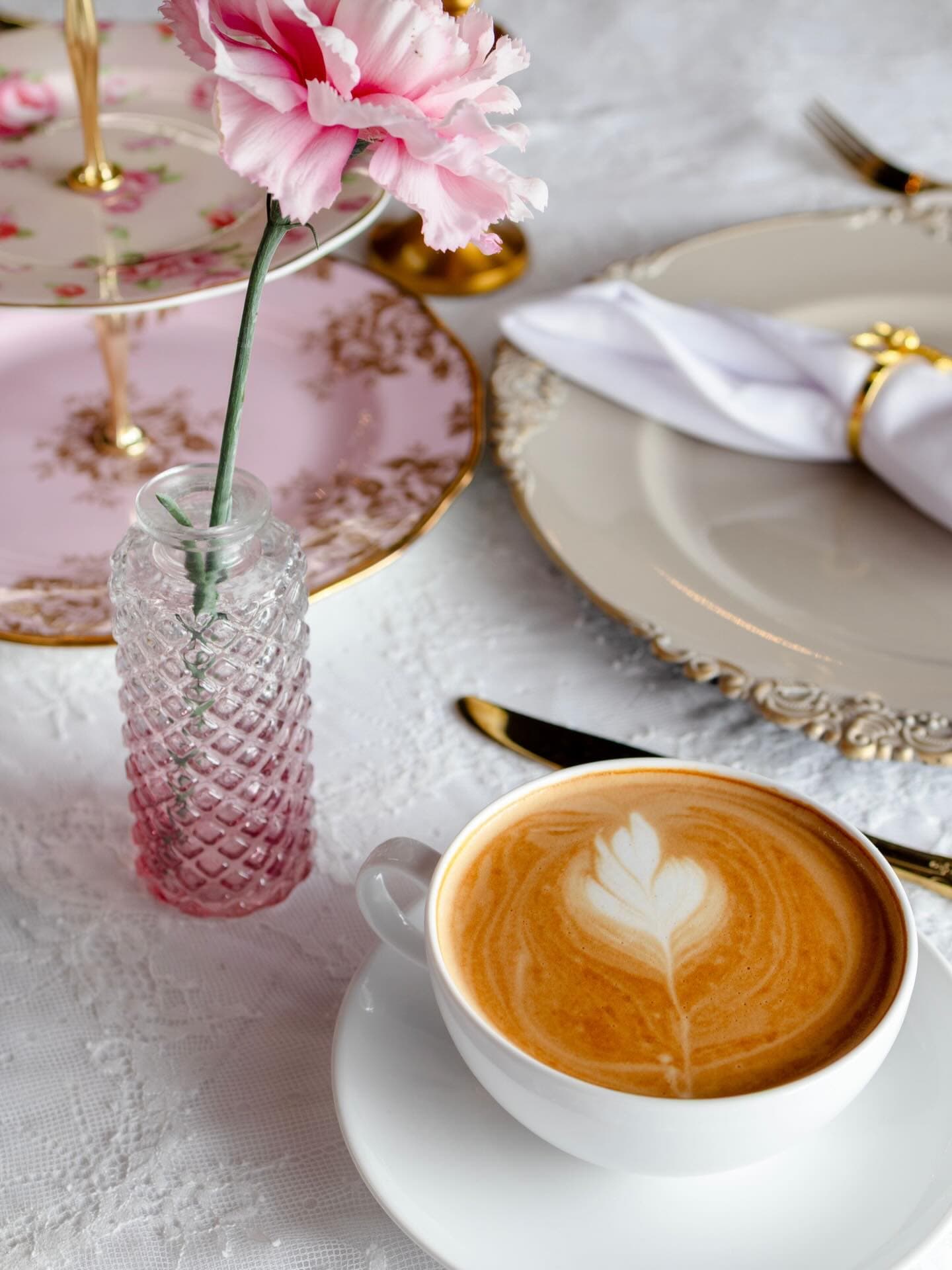 A latte, pink flower, patterned tea ware, and lace place setting.